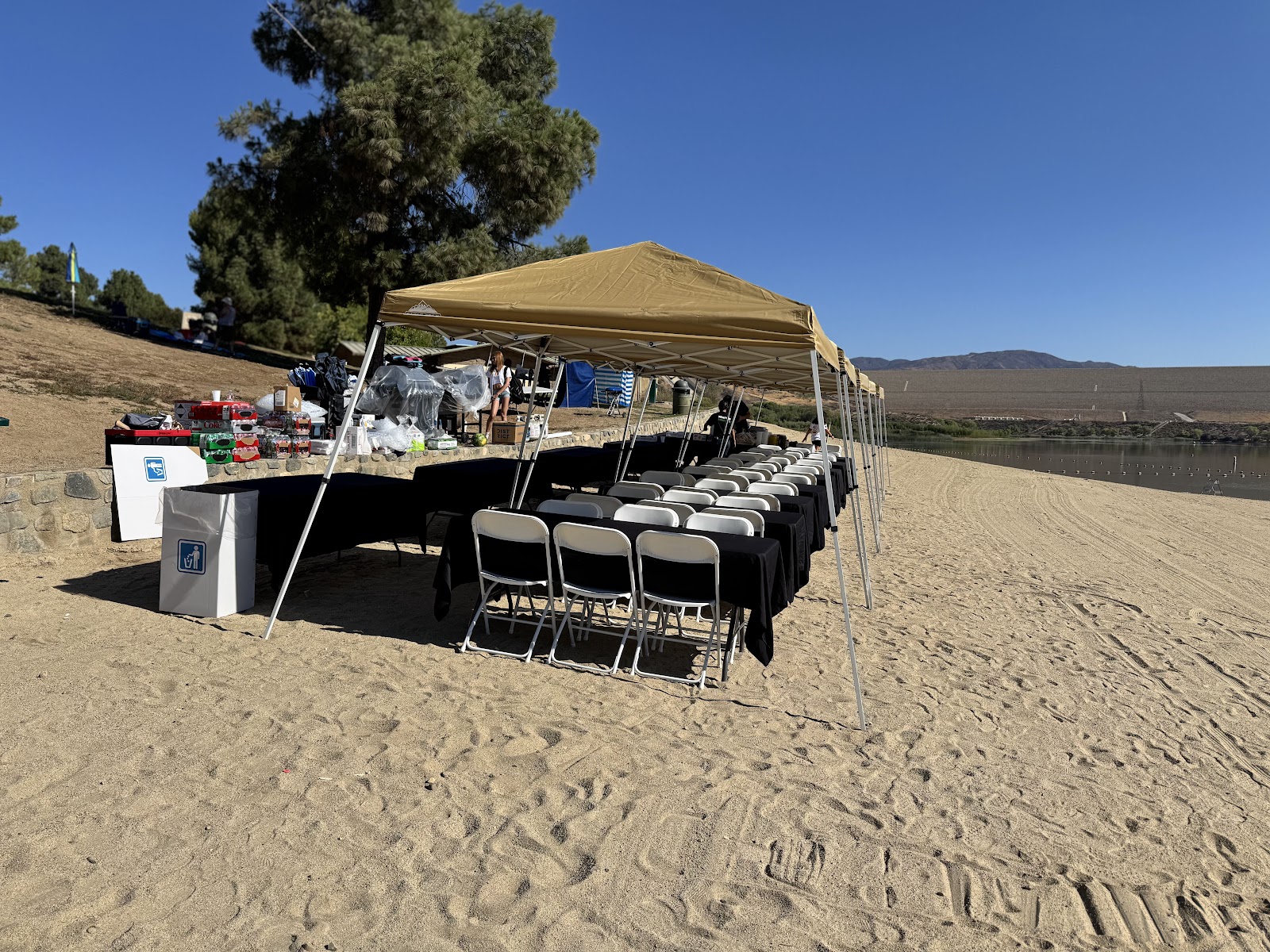 Lakeside party setup with tents, tables, black linens and white folding chairs